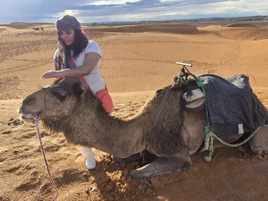 Travel agent Sophie Abdoollah petting a camel in a desert landscape with sand dunes in the background.